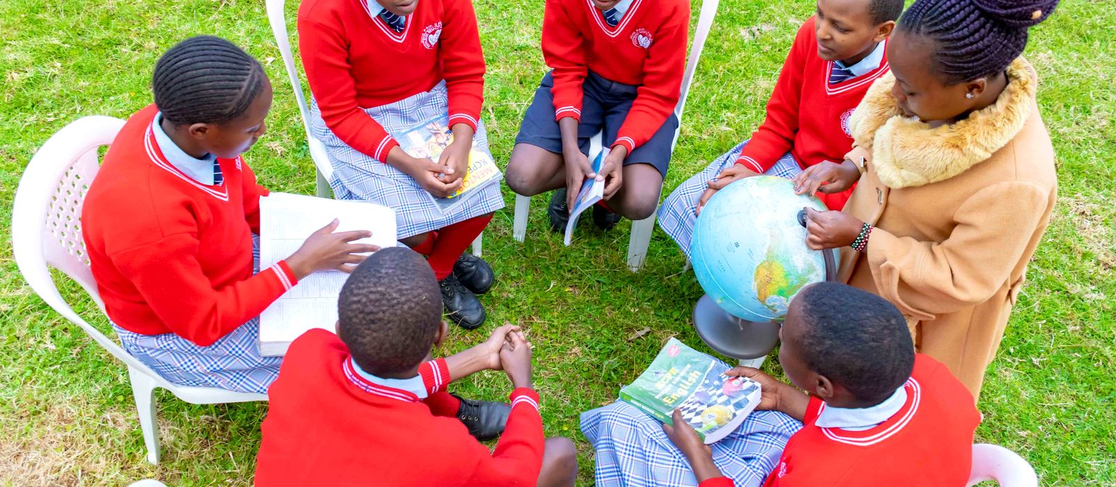 Learners in a group discussion around a globe with their teacher