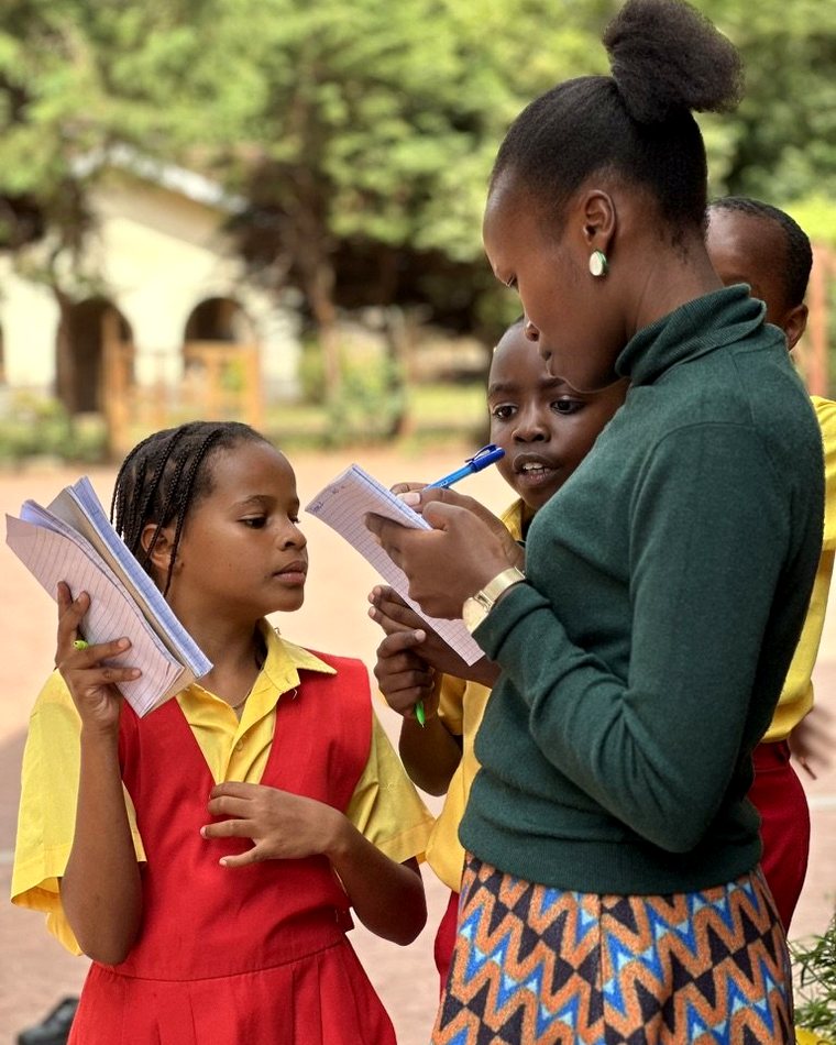 A teacher reviewing work with learners in a Kenyan school compound