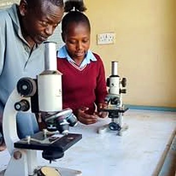 A teacher and student working with microscopes in a school laboratory